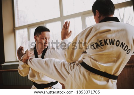 Two men practicing taekwondo together in the gym. People stand in the hall and practice martial arts techniques. 