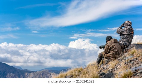 Two men in protective camouflage clothing on trophy hunt in the mountains. Hunter and the huntsman are searching in optical devices. - Powered by Shutterstock