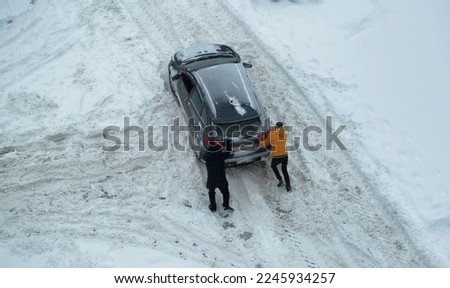 Two men push out a car stuck in the snow. The car skids in a snowdrift on an icy road. Uncleaned roads from snow.
