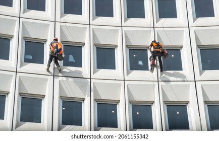 Two men rappelling from the wall for fix the damaged building in the city. Rappelling is a controlled descent off a vertical drop, such as a rock face, by descending a fixed rope.
