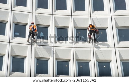 Two men rappelling from the wall for fix the damaged building in the city. Rappelling is a controlled descent off a vertical drop, such as a rock face, by descending a fixed rope.