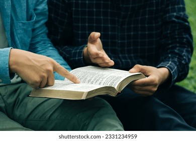 Two men read and studied the bible at the park and prayed together. sharing the gospel with a friend. Holy Bible study reading together on Sunday.Studying the Word Of God With Friends. Education. - Powered by Shutterstock