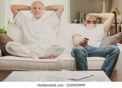 Two men relaxing at home, one older quietly meditating while listening to music and one younger laughing uproriously at a TV program