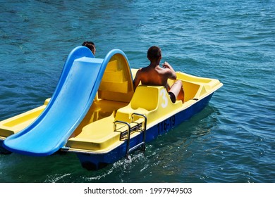 Two men ride a yellow catamaran in the sea. Friends pedal and row, so the catamaran moves away from the shore. The concept of male friendship, love, lgbt. Romantic sailing of two men on a catamaran