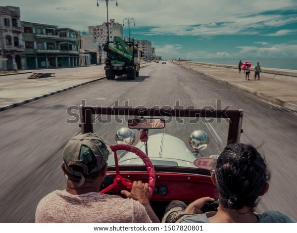 Two men riding / driving a\
white and red old convertible car (classical) In a warm sunny day\
with blue sky throw an old town.  (motion blur, speed, fun)\

