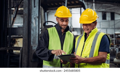 Two men in safety gear are looking at a tablet. One of them is pointing at something on the screen - Powered by Shutterstock