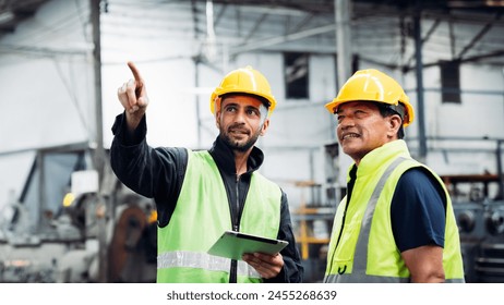 Two men in safety gear are pointing at something. One of them is holding a clipboard. Scene is serious and focused - Powered by Shutterstock