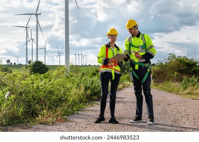 Two men in safety gear are standing on a road near a field of wind turbines. They are looking at something on their papers - Powered by Shutterstock