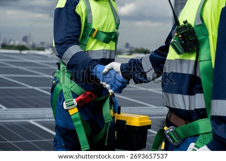 Two men shake hands while wearing safety gear. Scene is professional and serious. The idea of the image is that the two men are working together in a high-risk environment