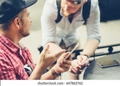 Two men share news, photos, video on the smartphone. A man shows a friend an application in a mobile phone. Friends with a smartphone, technology.
