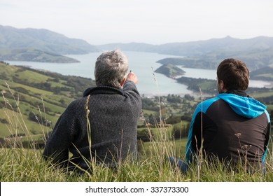 Two men sit on the top of hill and look at harbour, New Zealand