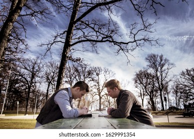 Two men sitting on a bench with bibles and praying in a garden under sunlight with a blurry background
