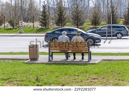 Two men are sitting on a bench near the road where cars drive