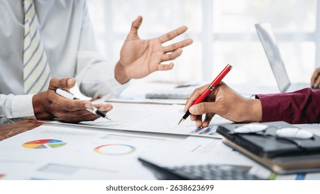 Two men are sitting at a table with a red pen and a white shirt. One of the men is writing on a piece of paper while the other man looks on