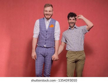 Two Men, Smiling And Happy Gay Couple Holding Hands Together, Shot In Studio Indoors (pink Background).