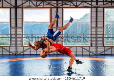 Two men in sports wrestling tights and wrestling during a traditional Greco-Roman wrestling in fight on a wrestling mat against the backdrop of mountains. Wrestler throws his opponent’s chest through