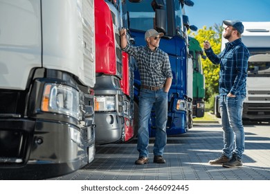Two men are standing next to several semi trucks lined up in a row. They appear to be inspecting the vehicles or discussing work-related matters.