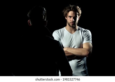 Two Men Standing Opposite. Focused Man, Serious Guy Having Conversation With Friend. Portrait Of A Serious Casual Men Standing With Arms Folded On Gray Background. Man In Shadow Dark.