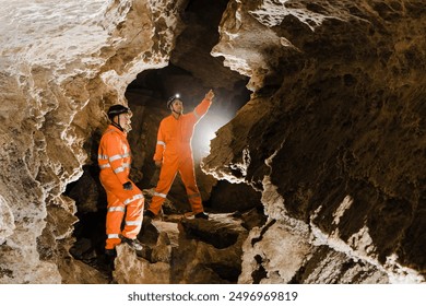 Two men, strong physique, explore the cave. Men dressed in special clothes to pass through the cave and stopped, looking at the map. - Powered by Shutterstock