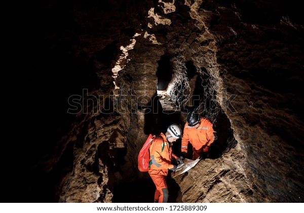 Two men, strong physique, explore the cave. Men\
dressed in special clothes to pass through the cave and stopped,\
looking at the map.