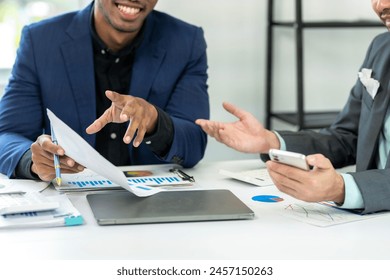 Two men in suits are talking about something on a table. One of them is holding a piece of paper and a pen