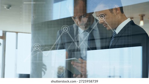 Two men in suits using tablet behind glass partition in office, showing reflected chart overlay. Colleagues, collaboration, data, graph, analytics, daylight, openplan - Powered by Shutterstock - Get 15% off with code: PIKWIZARD15