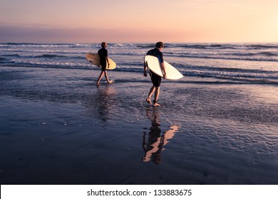 Two Men - Surfers in black diving suits. With old white and yellow surfboards. On the beach at sunset.