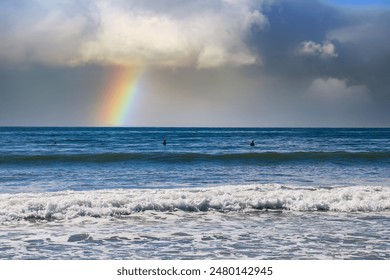 two men surfing on vast blue ocean water with waves rolling into the beach with blue sky, clouds and a rainbow at Rincon Beach in Ventura California USA	 - Powered by Shutterstock