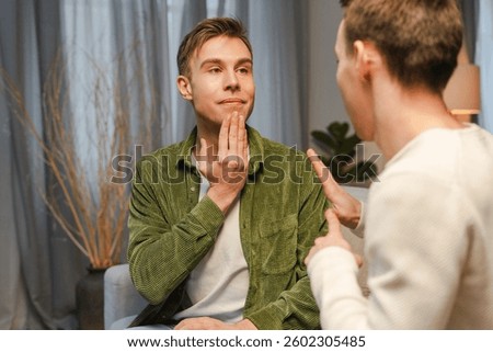 Two men are using sign language to communicate, practicing their skills in a comfortable home environment. Sign language concept