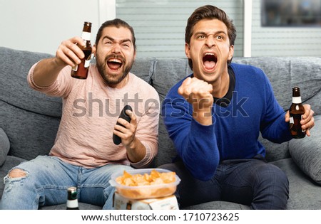 Two men watching matchup on tv drinking beer together at home