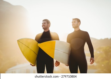 Two men in wetsuits with a surfboard on a sunny day at the beach - Powered by Shutterstock