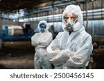 Two men in white protective gear stand in a factory. One of them is wearing a gas mask