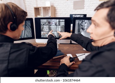 Two men work as guards. They sit in front of the monitors in the security room. The headphones are on their heads.