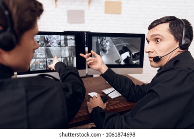 Two men work as guards. They sit in front of the monitors in the security room. The headphones are on their heads.
