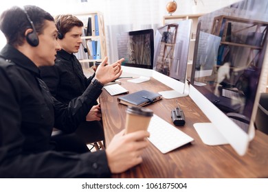 Two men work as guards. They sit in front of the monitors in the security room. The headphones are on their heads.