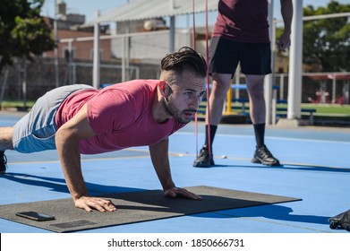 Two Men Working Out Together At Outdoors, Two Male Doing Planks, Push Ups And Working Out With Resistance Bands. People Adapting To The New Normal Outside. 