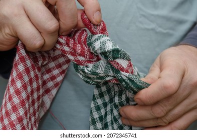 Two Men's Hands Tie Two Towels Together. Knotted Red And Green Checkered Kitchen Napkins. Selective Focus.