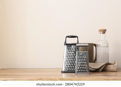 Two metal graters with kitchenware on wooden table