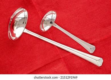 Two Metal Ladles On A Red Linen Napkin, Macro, Top View.