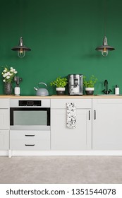 Two Metal Lamps Above Kitchen Counter With Herbs, Coffee Maker And Roses In Vase, Copy Space On Empty Green Wall