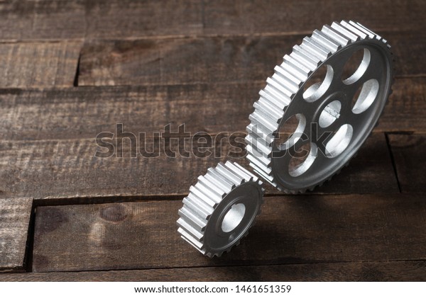 Two metal silver gears lies on old\
weathered wooden table in workshop. Copy space for\
text