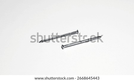 Two metallic nails placed on a plain white surface.
