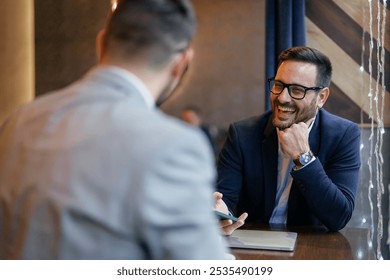 Two mid adult Caucasian males in suits engage in a productive discussion at a cafe, one holding a smartphone, with professional focus in a casual setting. - Powered by Shutterstock