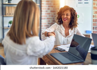 Two middle age beautiful businesswomen smiling happy and confident working together. Shaking hands with smile on face for agreement at the office