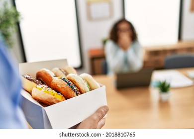 Two middle age business workers working at the office. Man holding box with doughnuts to his partner. - Powered by Shutterstock