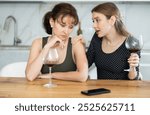 Two middle-aged ladies sitting having wine in goblets while one consoling another looking sorrowful