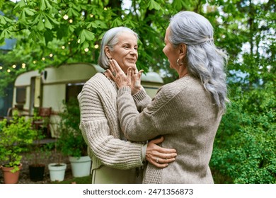 Two middle-aged women in cardigans embrace warmly outdoors. - Powered by Shutterstock