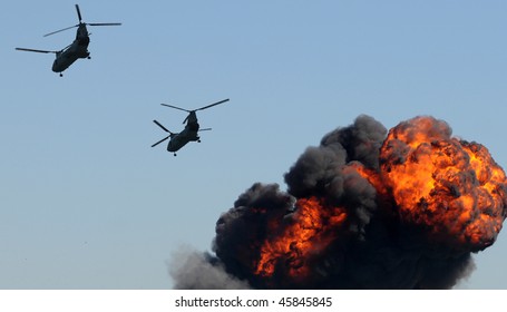 Two Military Helicopters Flying Over Fiery Explosion And Smoke