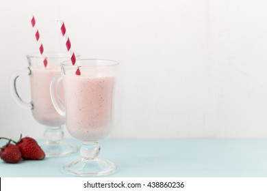 Two milk shakes with strawberries, ice-cream pink cocktail with straws on blue wooden table, copy space at right, top view