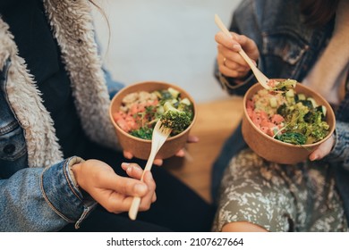 Two Millennial Women Female Friends Sitting Outdoors Eating Takeaway Food, Laughing And Having Fun. Food Delivery And Takeout.